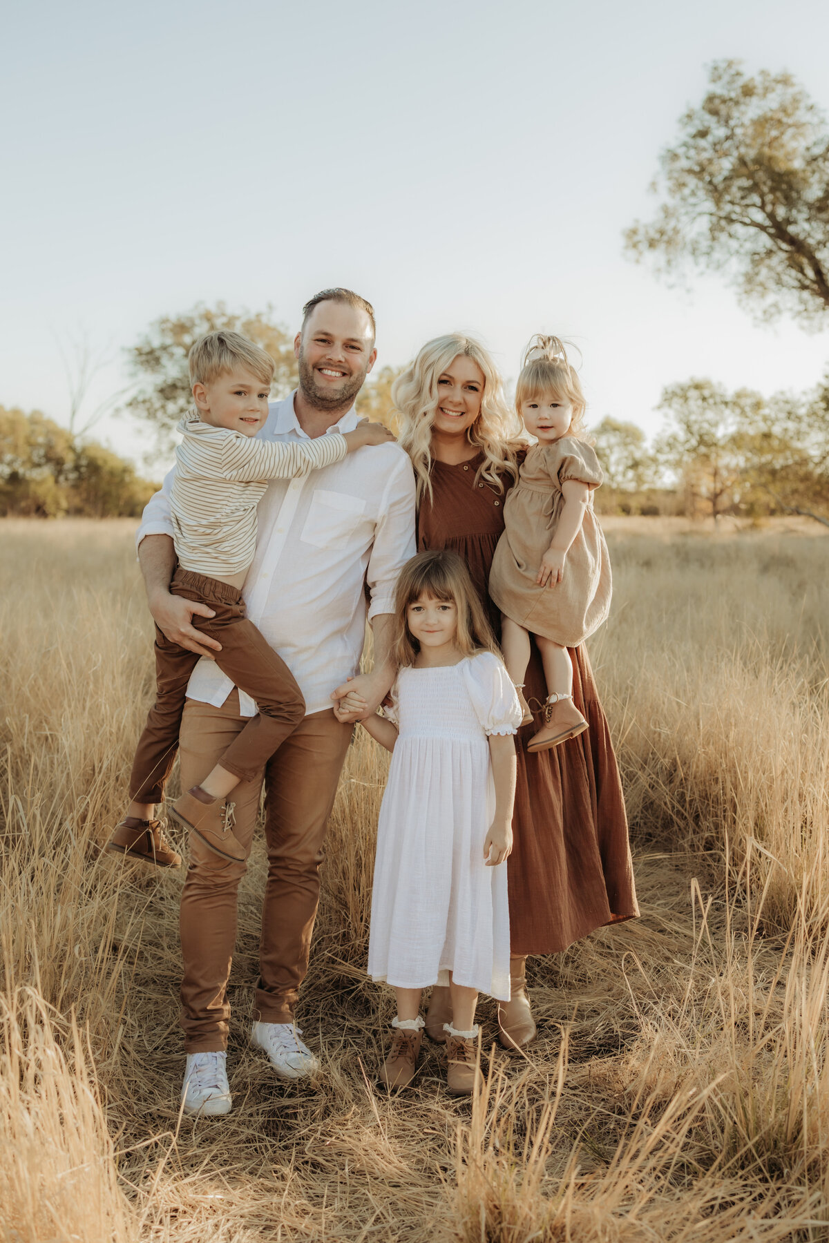 A family cuddled together looking at the camera in a golden field in Perth WA