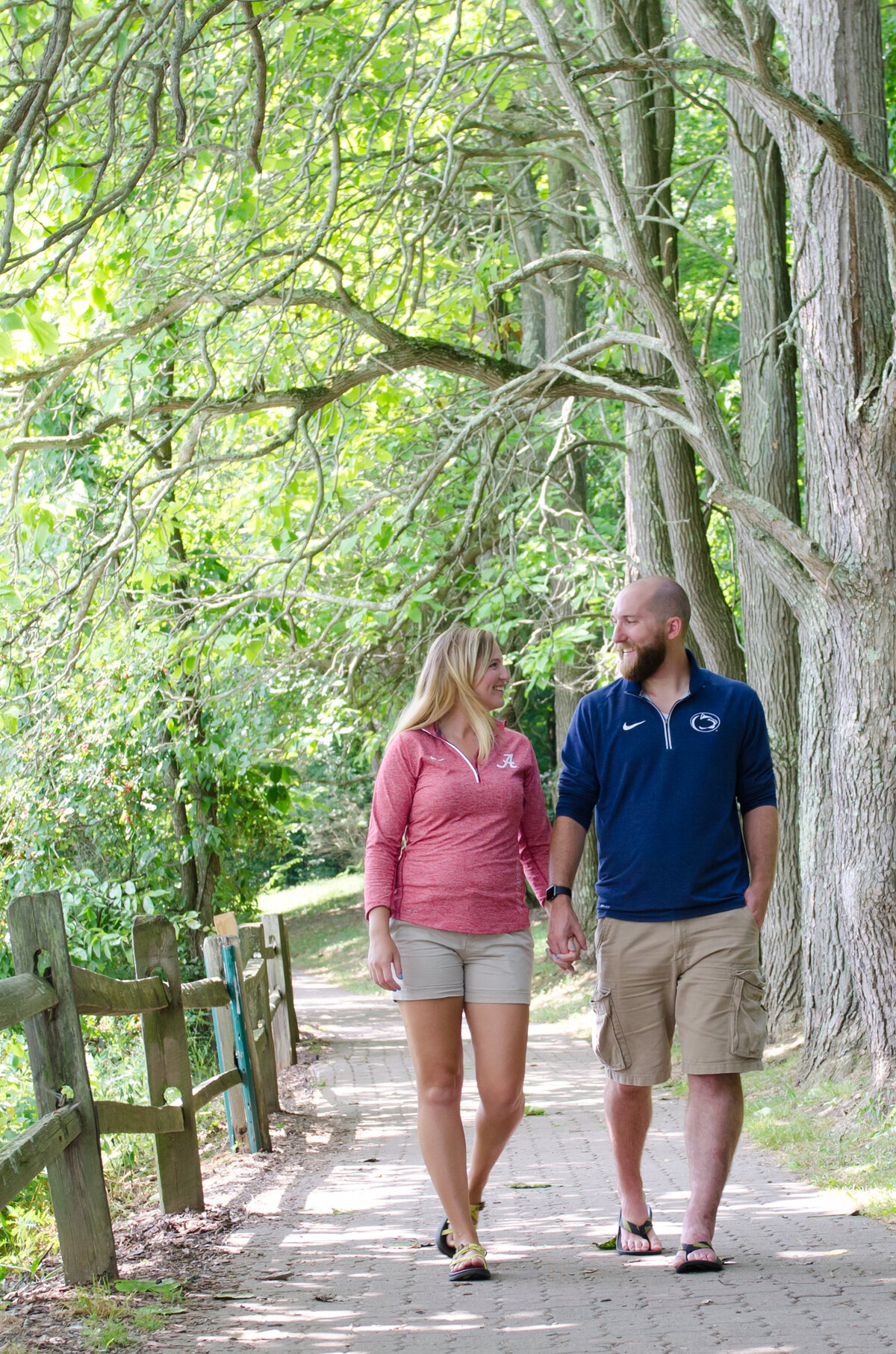 An engaged couple walks along a tree-lined brick walkway at Twin Lakes Park in Greensburg, PA