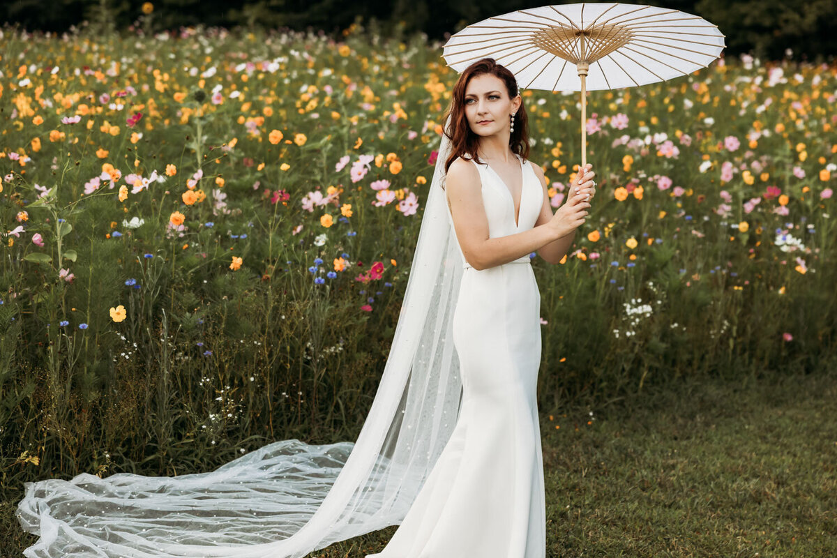 Bride in white gown holding parasol in a flower field