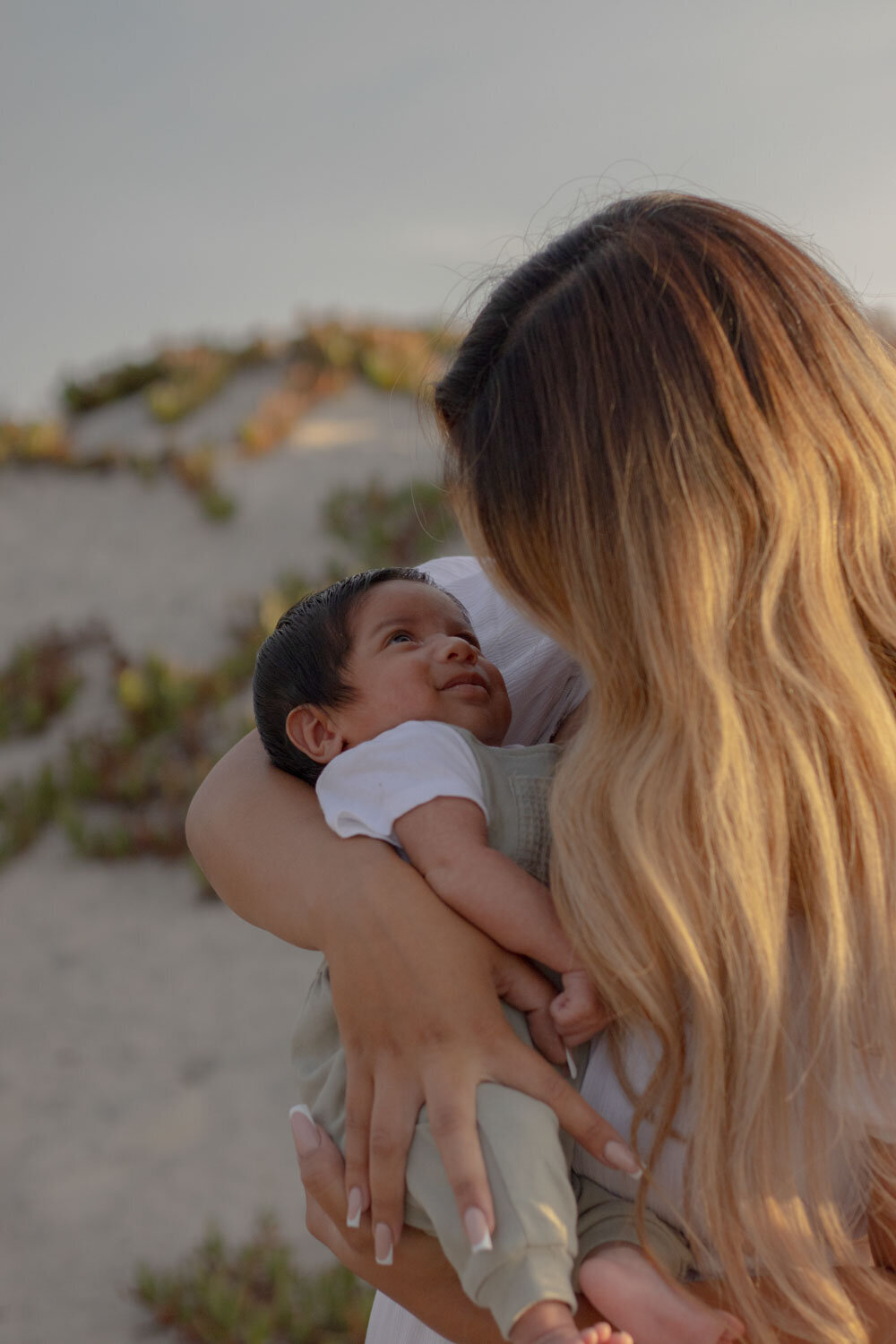A mother holding her newborn baby close, gazing lovingly at each other during a family beach session