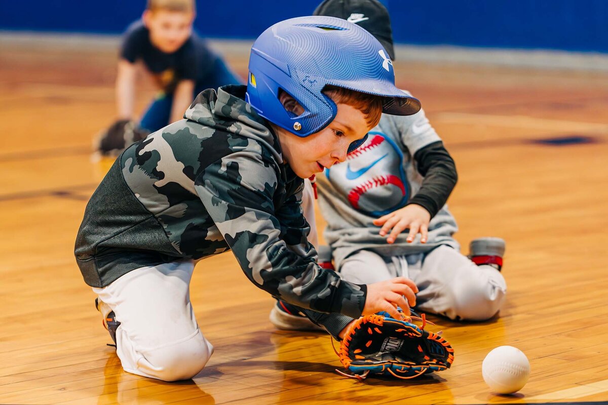 Little boy blue reaching for ball at tee ball practice