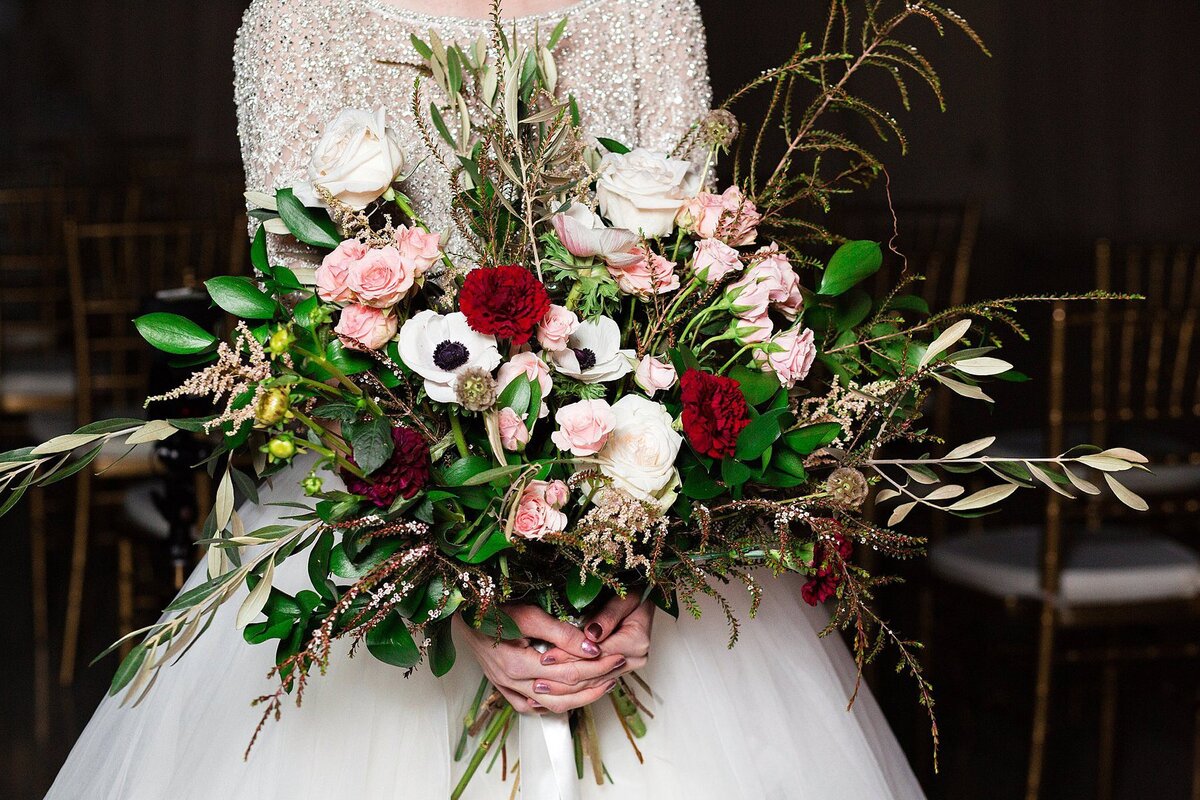 Large horizontal cascade bouquet of pink carnations white anemone, red carnations, pink roses, red roses, white roses, and assorted greenery with eucalyptus.