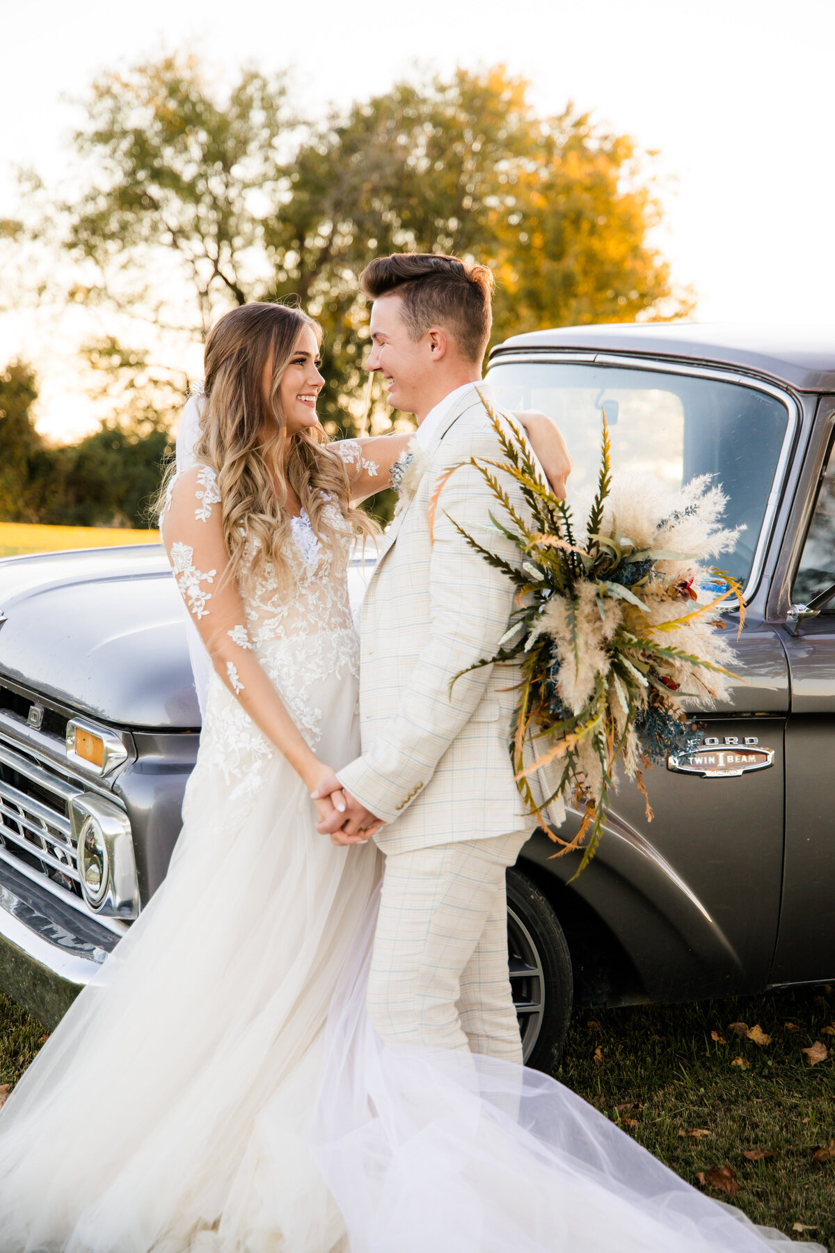 Bride and Groom holding hands looking at each other standing in front of a vintage truck