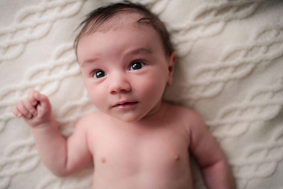 Awake newborn baby lying on a soft textured blanket, looking up with wide open eyes.