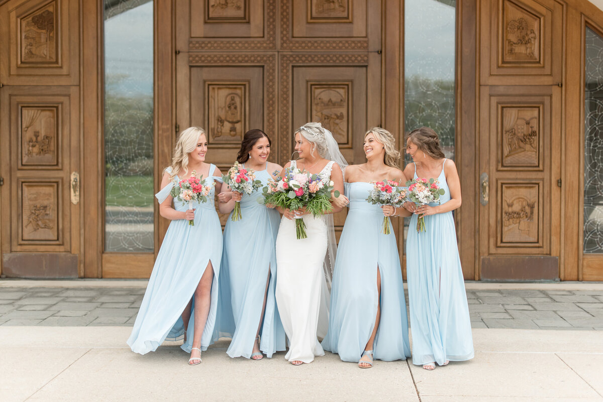 Bride surrounded by her four bridesmaids in baby blue dresses outside large church door in Maryland.