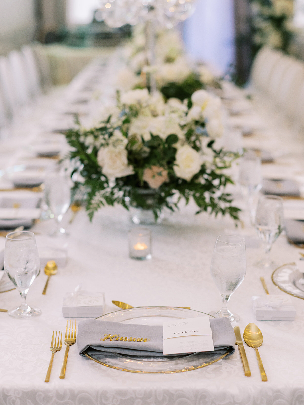 A long dining table is elegantly set with white linens, gold utensils, glass plates, and floral centerpieces. Place settings include menus and name cards—a perfect setup for a classic Calgary wedding at the Fairmont Palliser.