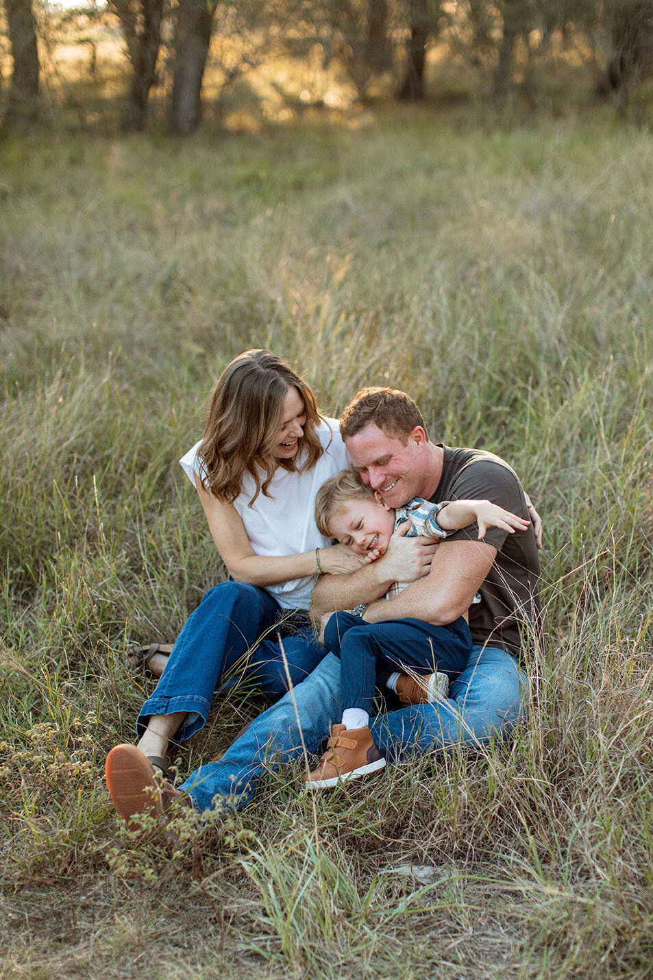Family embracing in group hug outdoors in field - Sara James captures heartwarming family connections and togetherness during professional portrait sessions in San Antonio Texas
