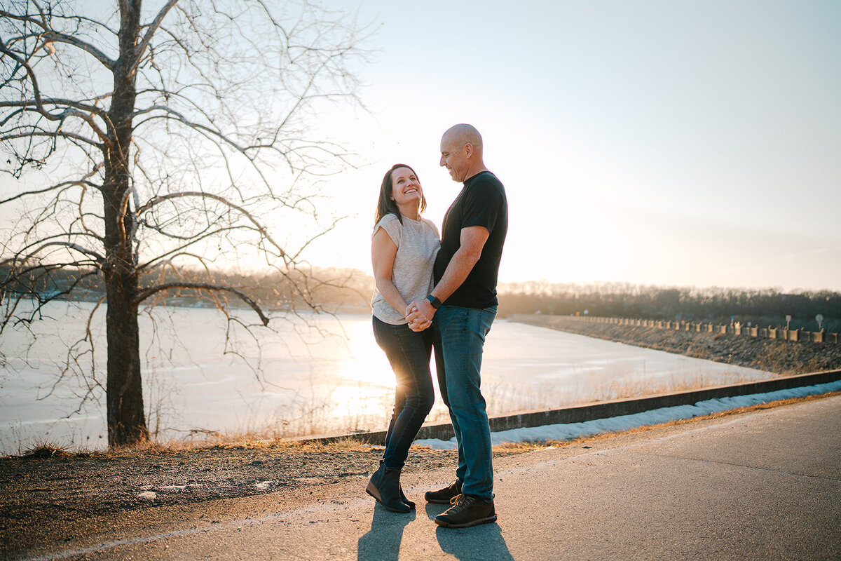 A couple holding hands and smiling while standing in front of a lake. 