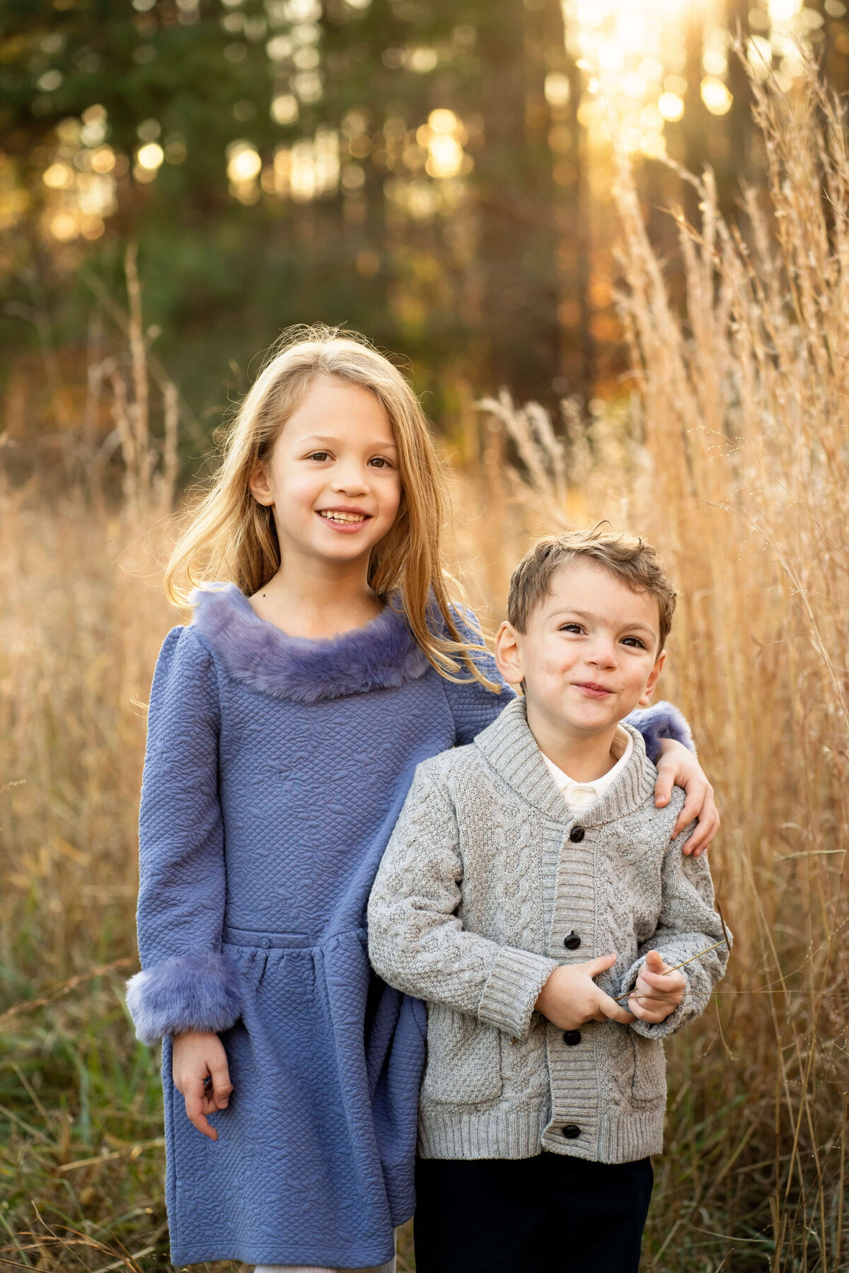 Young brother and sister smiling at camera in field of tall grass