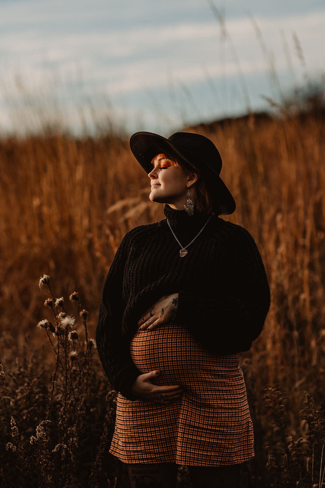 A pregnant person holding their stomach and standing in a tall grassy field 