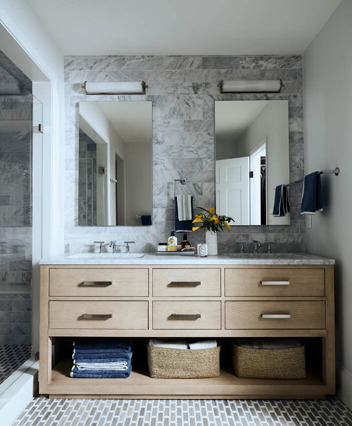 Explore the classic primary bathroom in a historic Hingham home, featuring an oak vanity, mosaic tile flooring, and a walk-in shower with Carrara marble wall tiles.