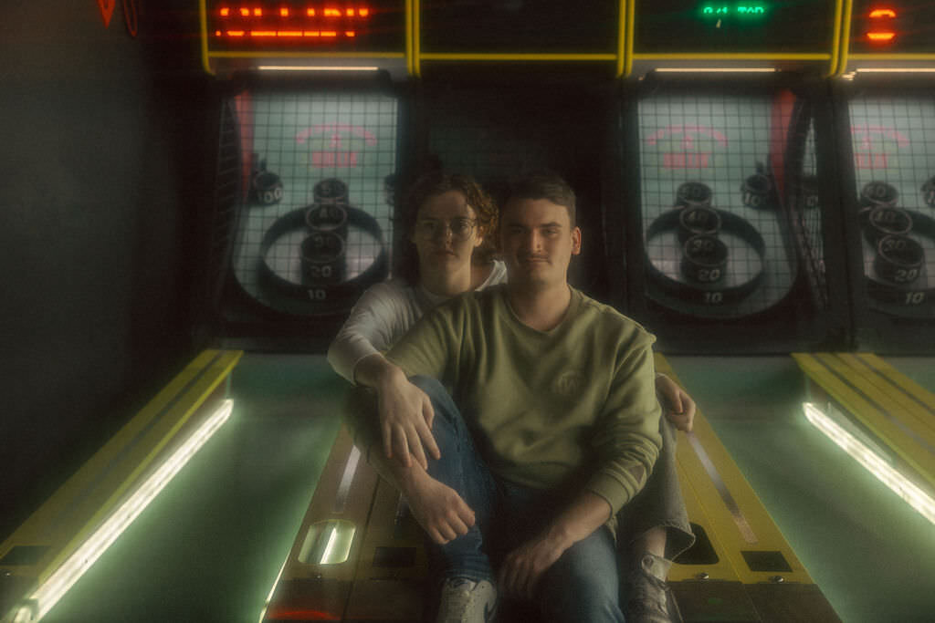 Two people sitting on a ski ball machine.