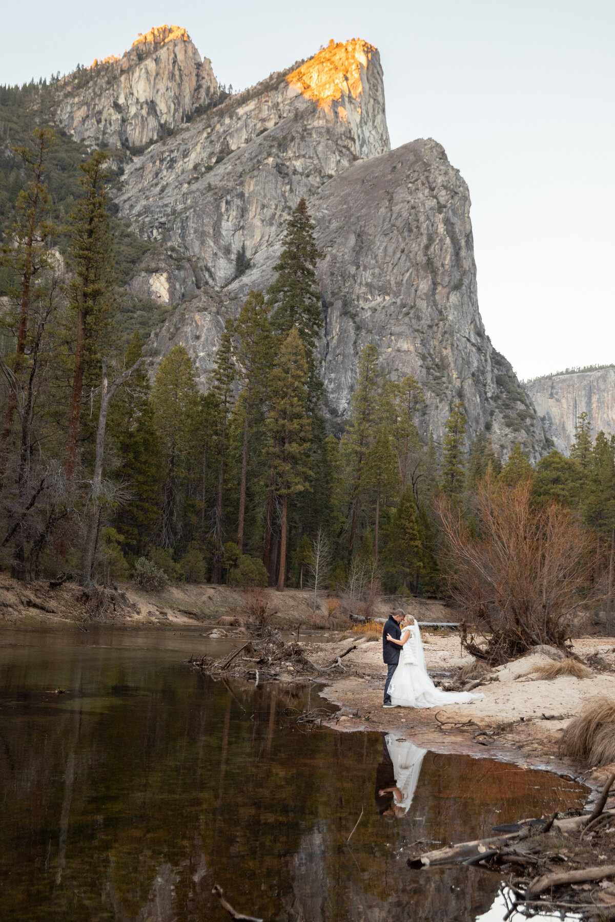 A bride and groom share their first dance on a beach in Yosemite as the mountains tower behind them.
