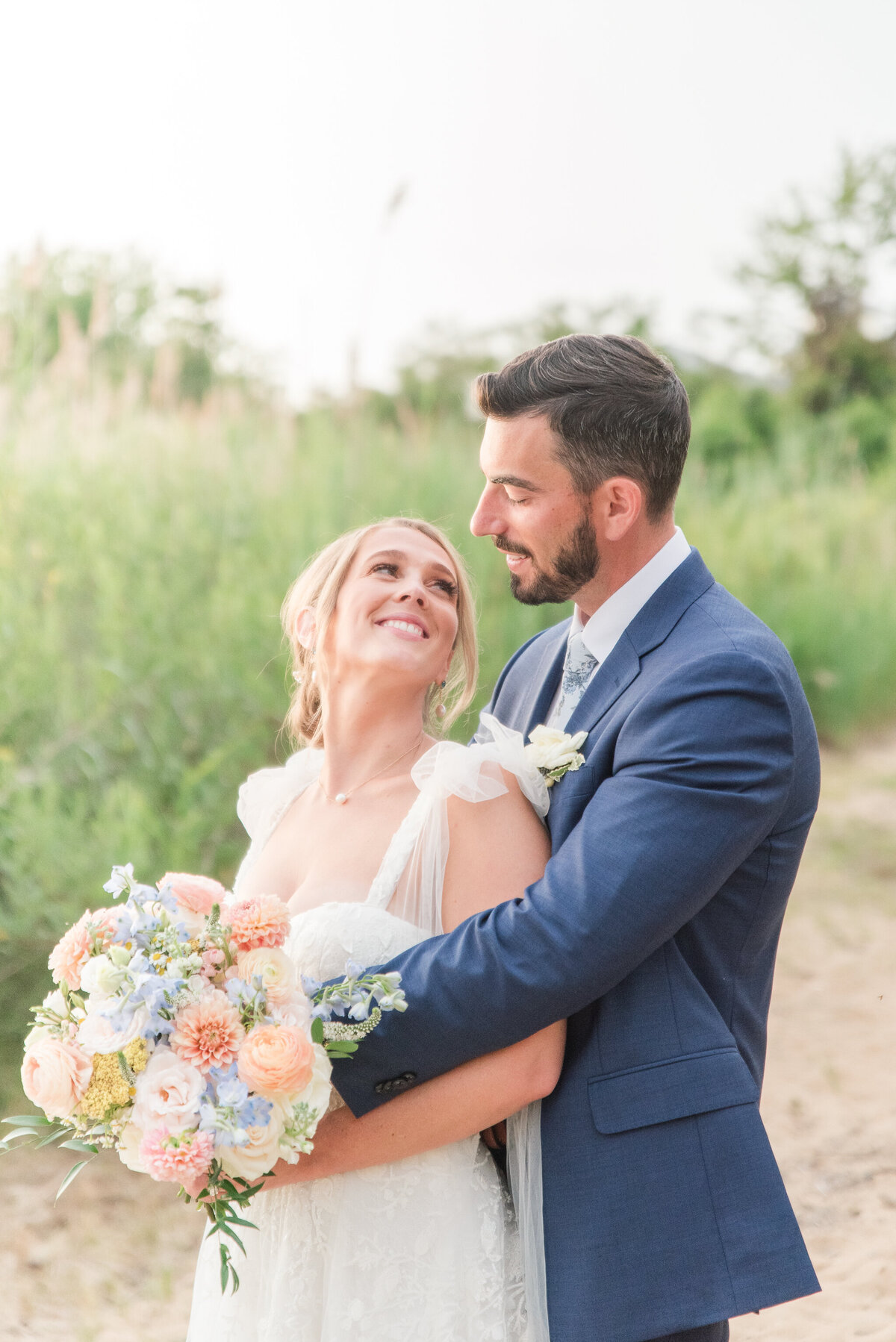 bride and groom looking into each other's eyes in a blue suit with floral tie and peach blue bouquet