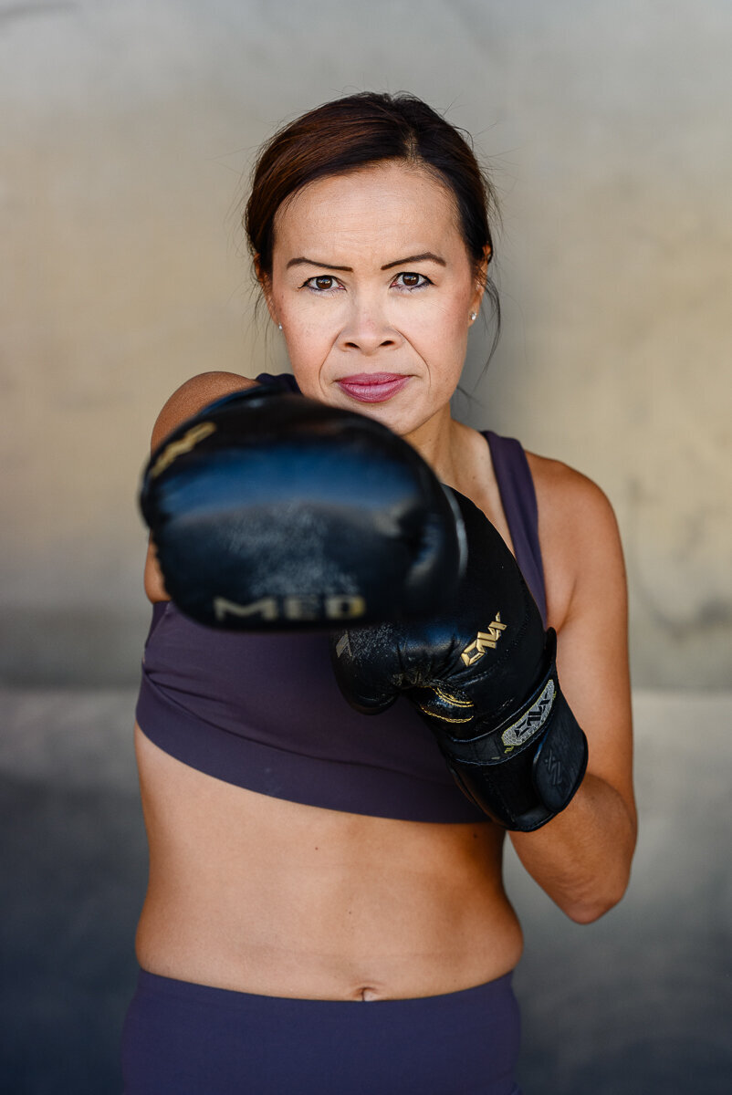Branding photos in Denver for a woman Dr. of weightloss punching with boxing gloves toward a branding photographer in Denver.