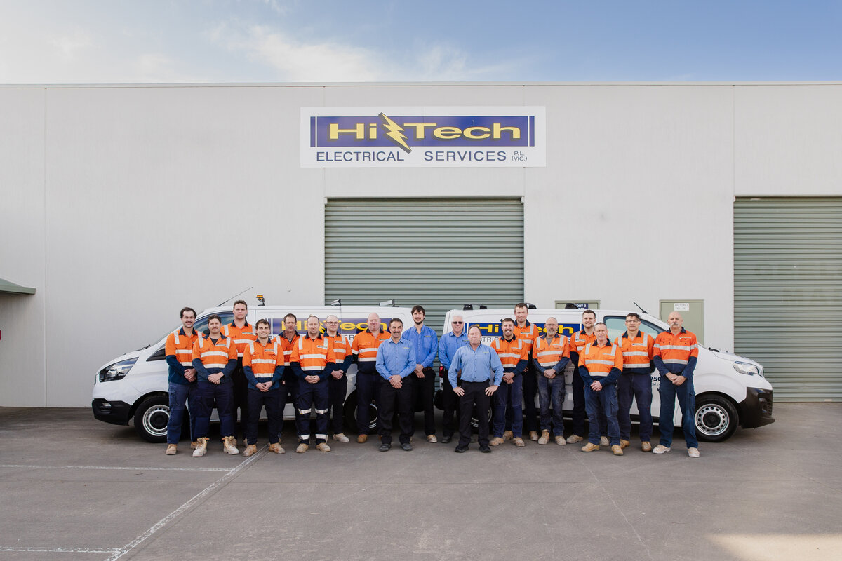 20+members of the industrial electrical contractors Hi Tech team standing outside of  white warehouse with Hi Tech Sign