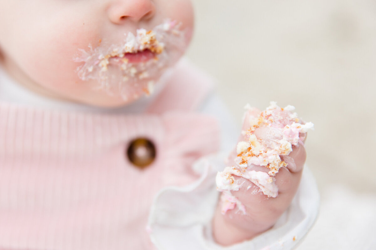 Close up image of baby's hand covered in frosting during cake smash session on beach at Lake Lanier