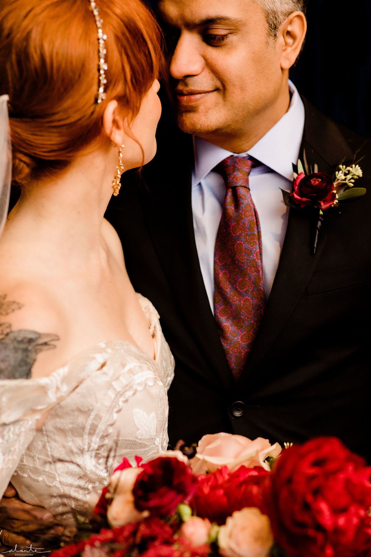 Groom looking at bride holding deep red bridal bouquet