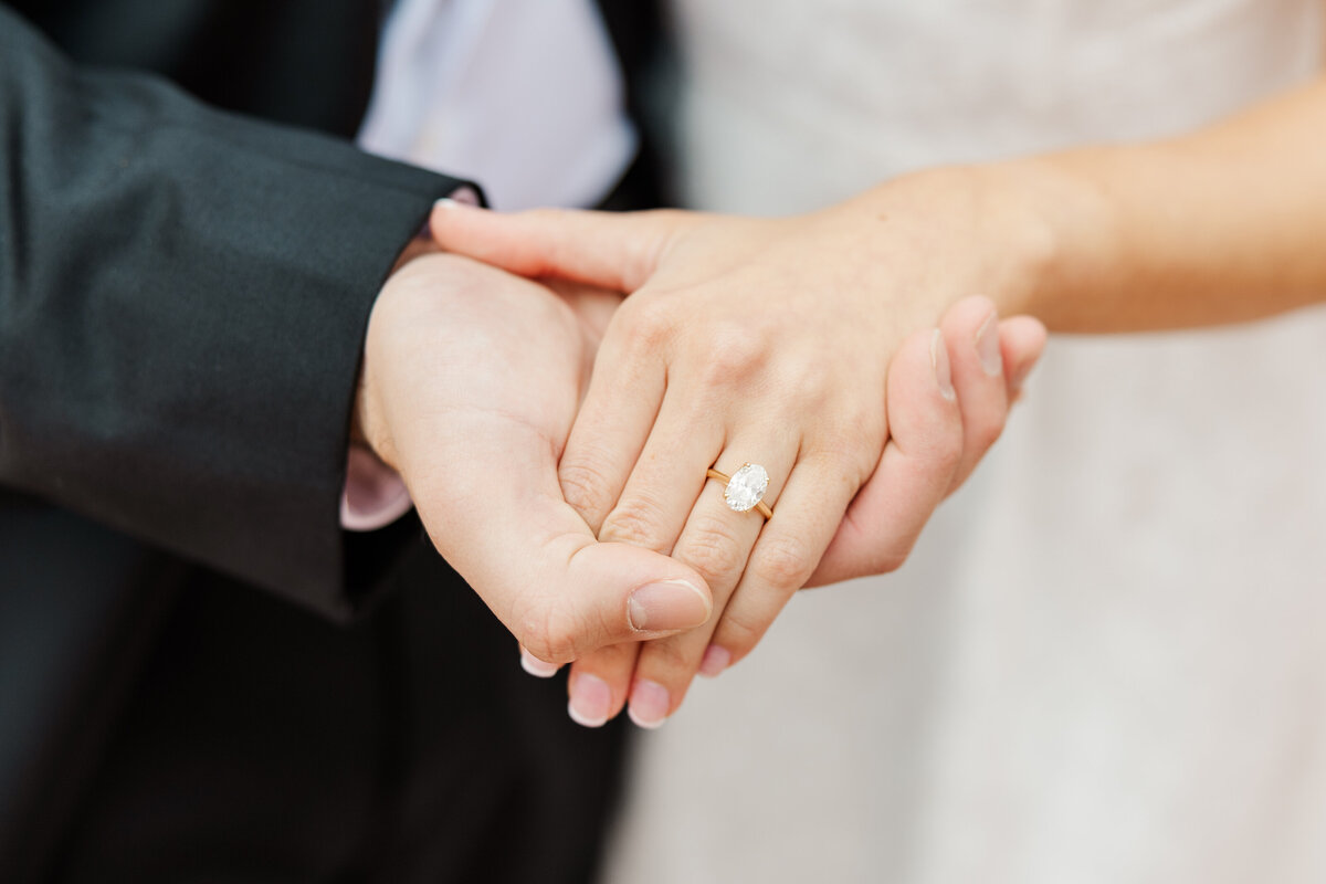 A romantic detail shot of a couple’s hands during their Downtown Fort Worth engagement session. The bride-to-be’s oval diamond ring sparkles on a gold band as the groom gently holds her hand. Elegant and timeless portrait capturing love and commitment in the heart of the city.