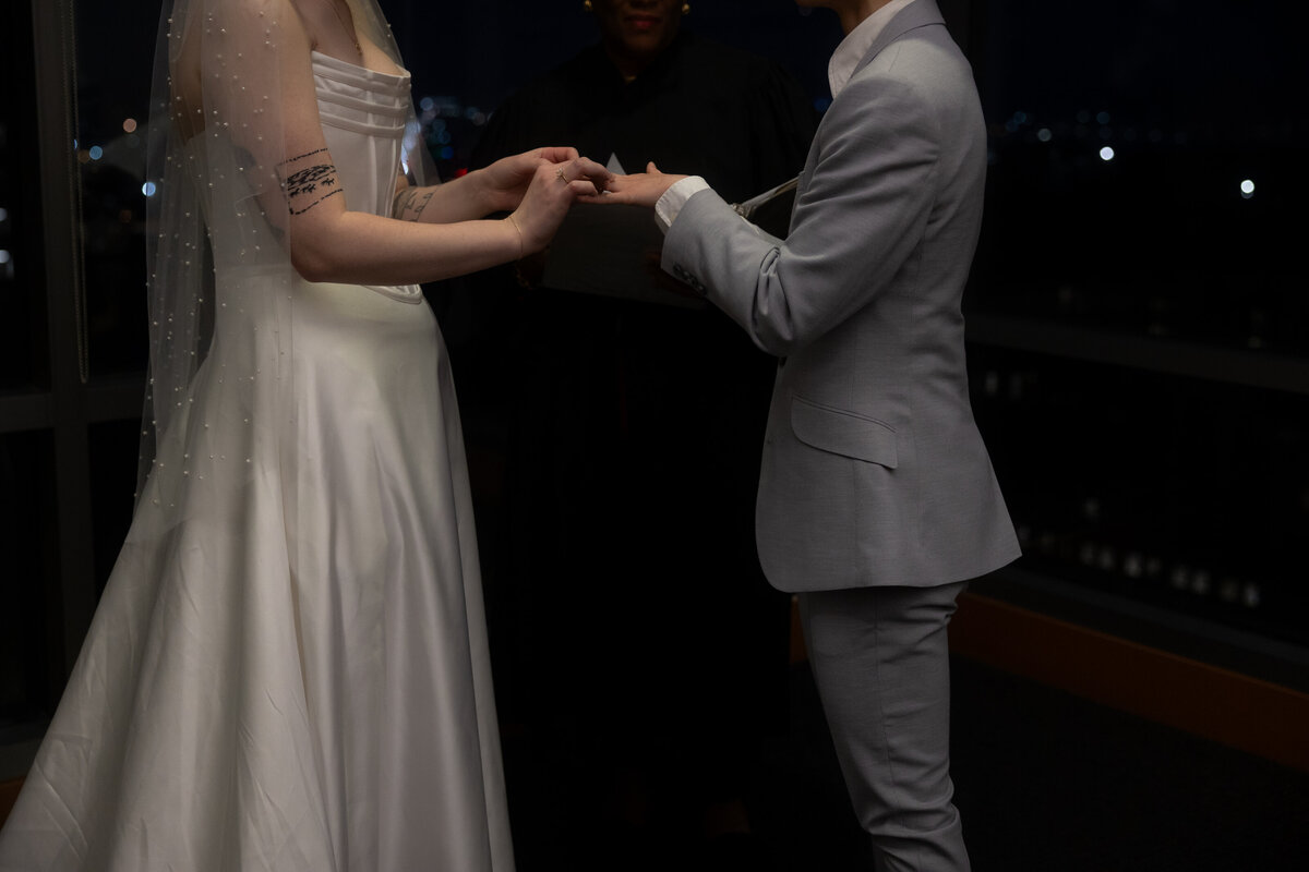 A heartfelt moment as the bride carefully places the engagement ring on her fiancé’s finger, symbolizing their commitment and love during their wedding ceremony at Seattle Courthouse.