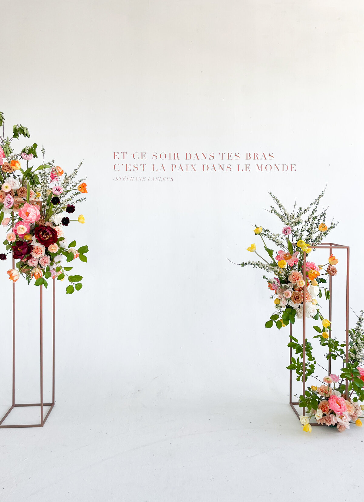 A pair of colourful, airy ceremony arrangements against a white wall for a wedding at L’Eloi.