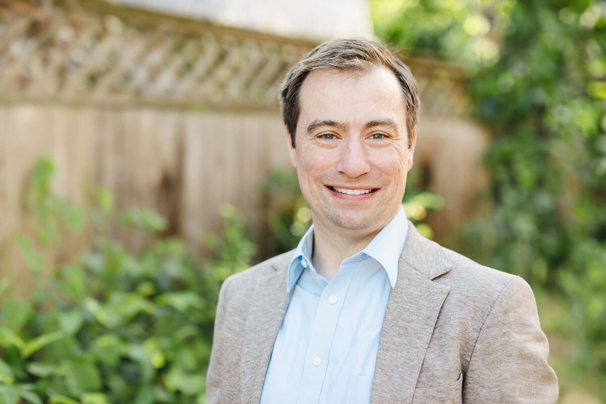 A person smiles in a tuxedo surrounded by a picket fence.