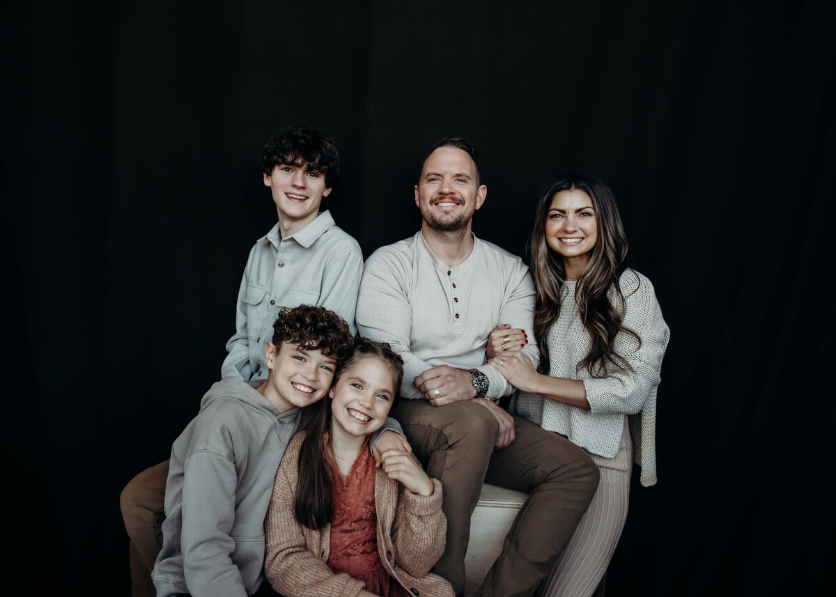 family of 5 smiles at camera with black background