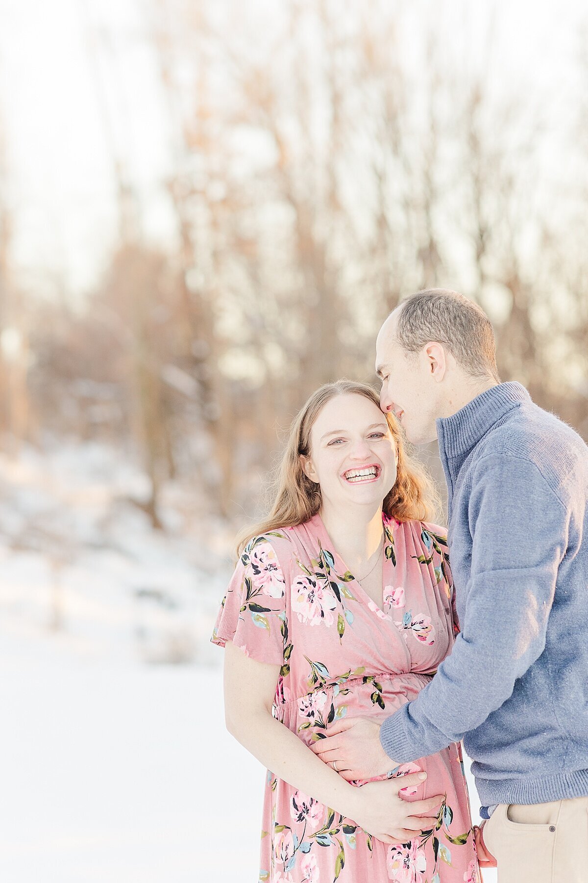 couple laughs during snowy winter maternity photo session with Sara Sniderman Photography in Medfield Massachusetts