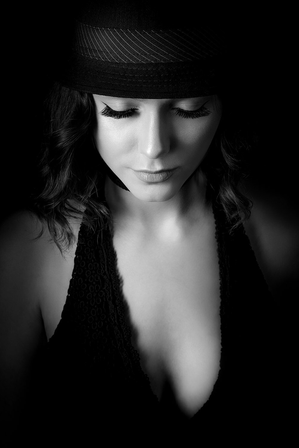 Striking low-key studio portrait of a woman in a black dress and fedora, lit in a dramatic cinematic style.