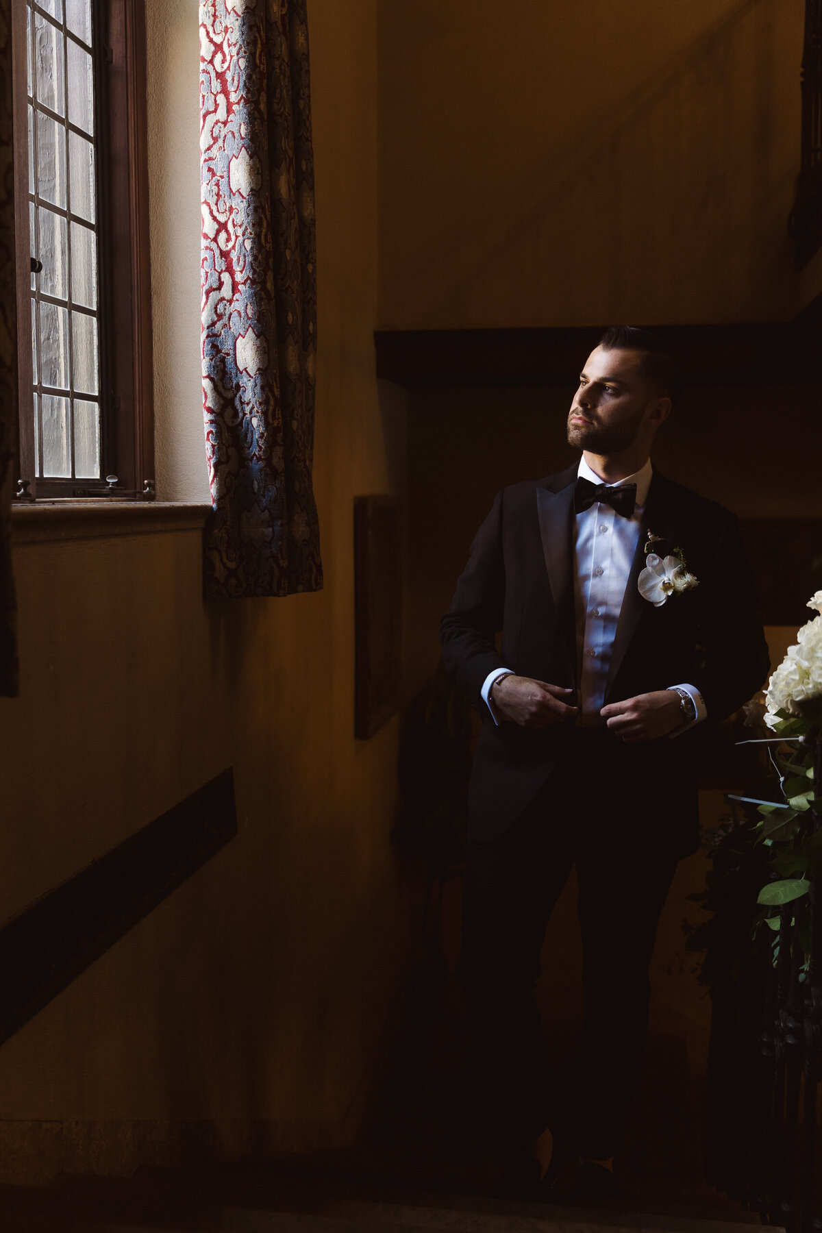 creative window light portrait of the groom walking up stairs