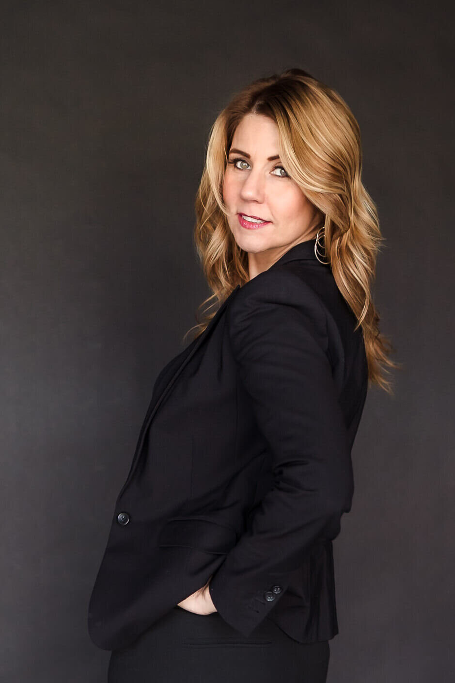 Smiling woman with long blonde hair in black top against dark studio backdrop