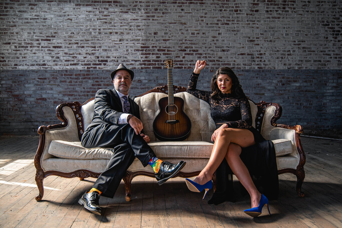 Two people sitting on a couch together with a guitar in between them 