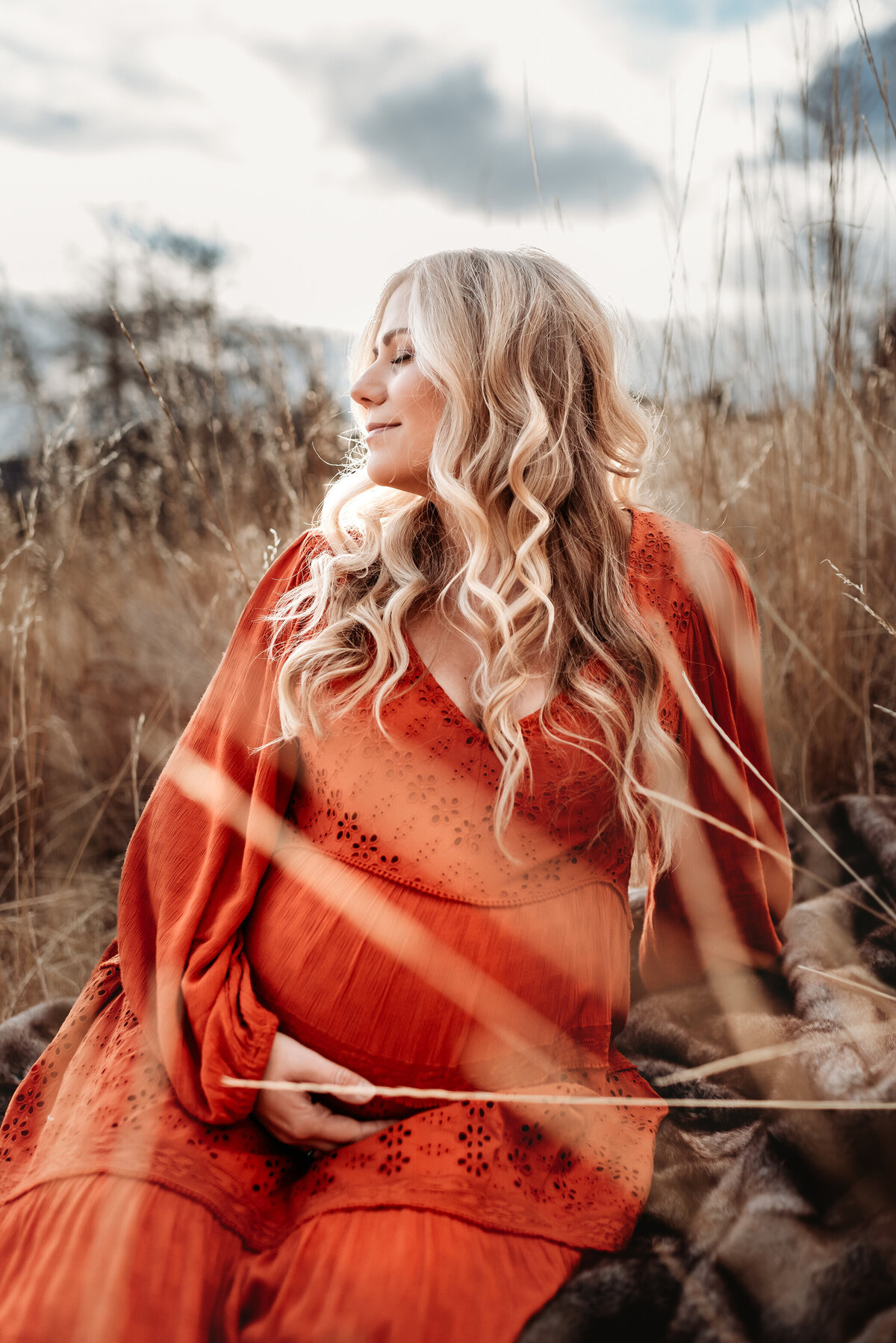blonde woman sitting in golden grass looking to the side