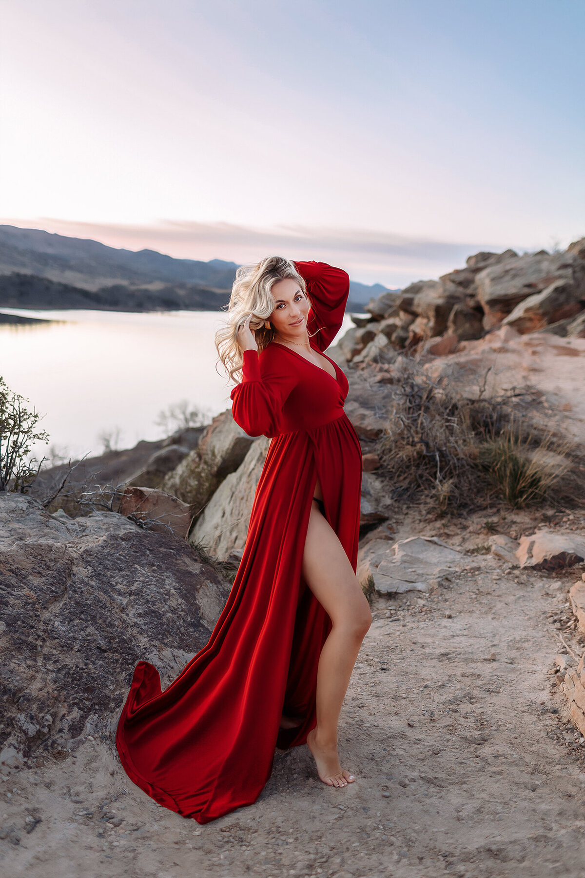 gorgeous pregnant mom in a red maternity gown posed on the cliffs at horsetooth reservoir in fort collins co for maternity photos