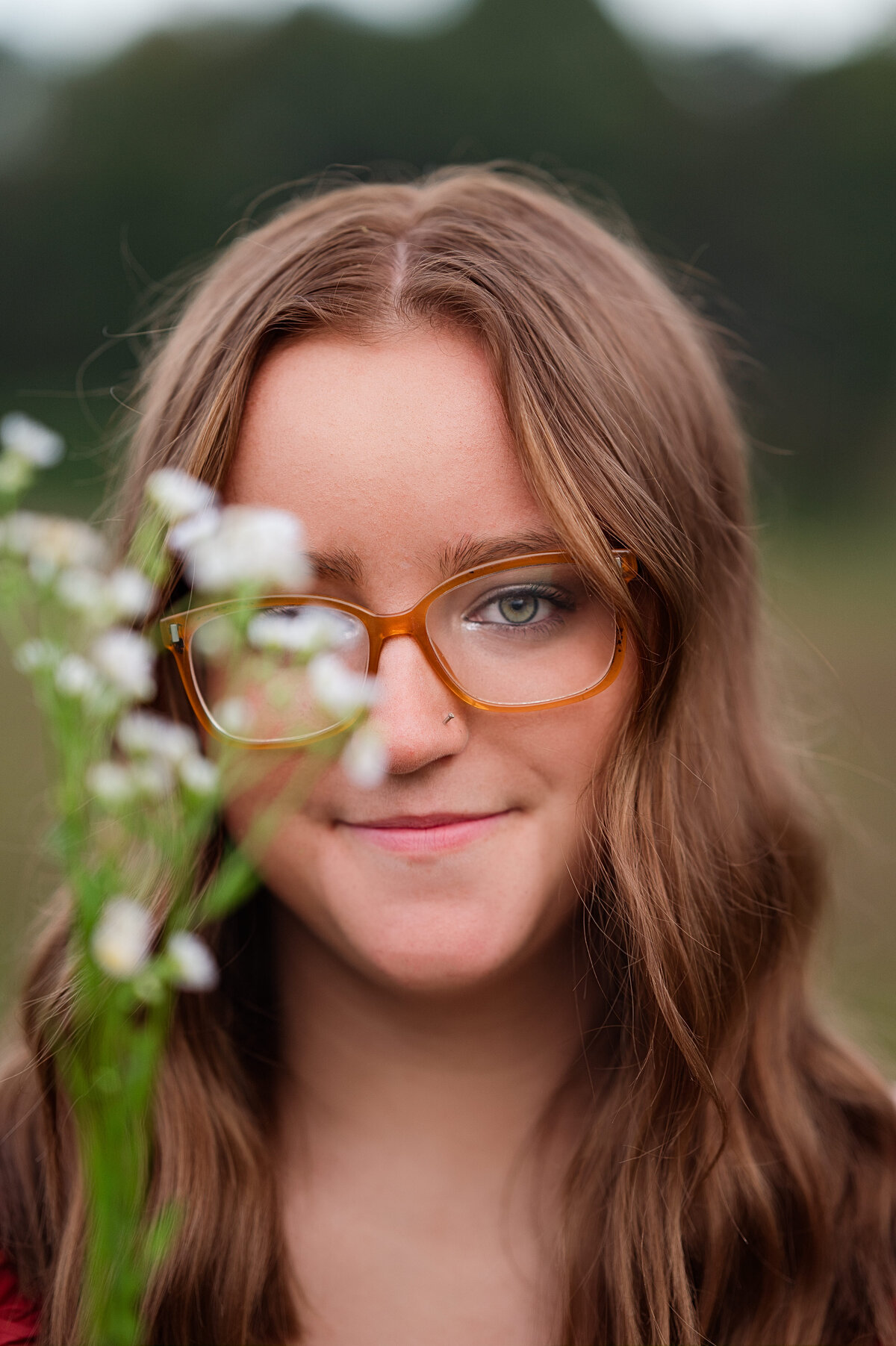 Beautiful brunette holds a small handful of white flowers by her face and looks directly into the camera during her senior session at Prospect Farms