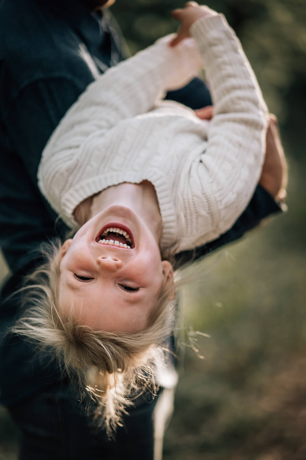 A close up photo of a little girl laughing while being held upside down by her father.