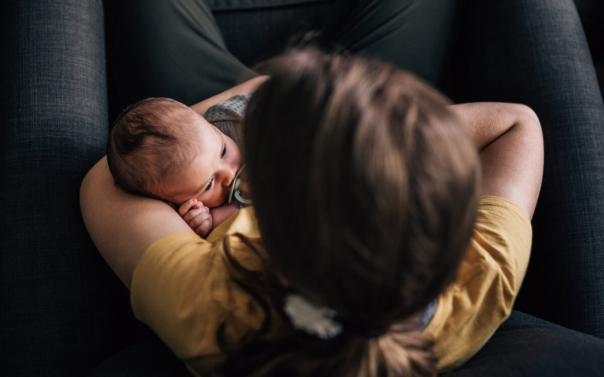 An in home photo session with newborn photographer, Kate Simpson, in which an older sibling holds her brand new baby brother as he gazes straight into her eyes.