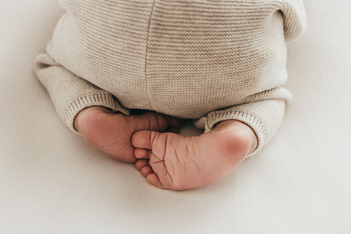 A sweet close-up focusing on the small feet and legs of a newborn baby dressed in a cozy cream knit. Newborn photography services by Ruaa Hamdan in Altrincham
