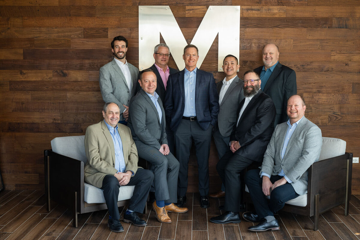 A group of men are posing for a picture in front of a large letter M