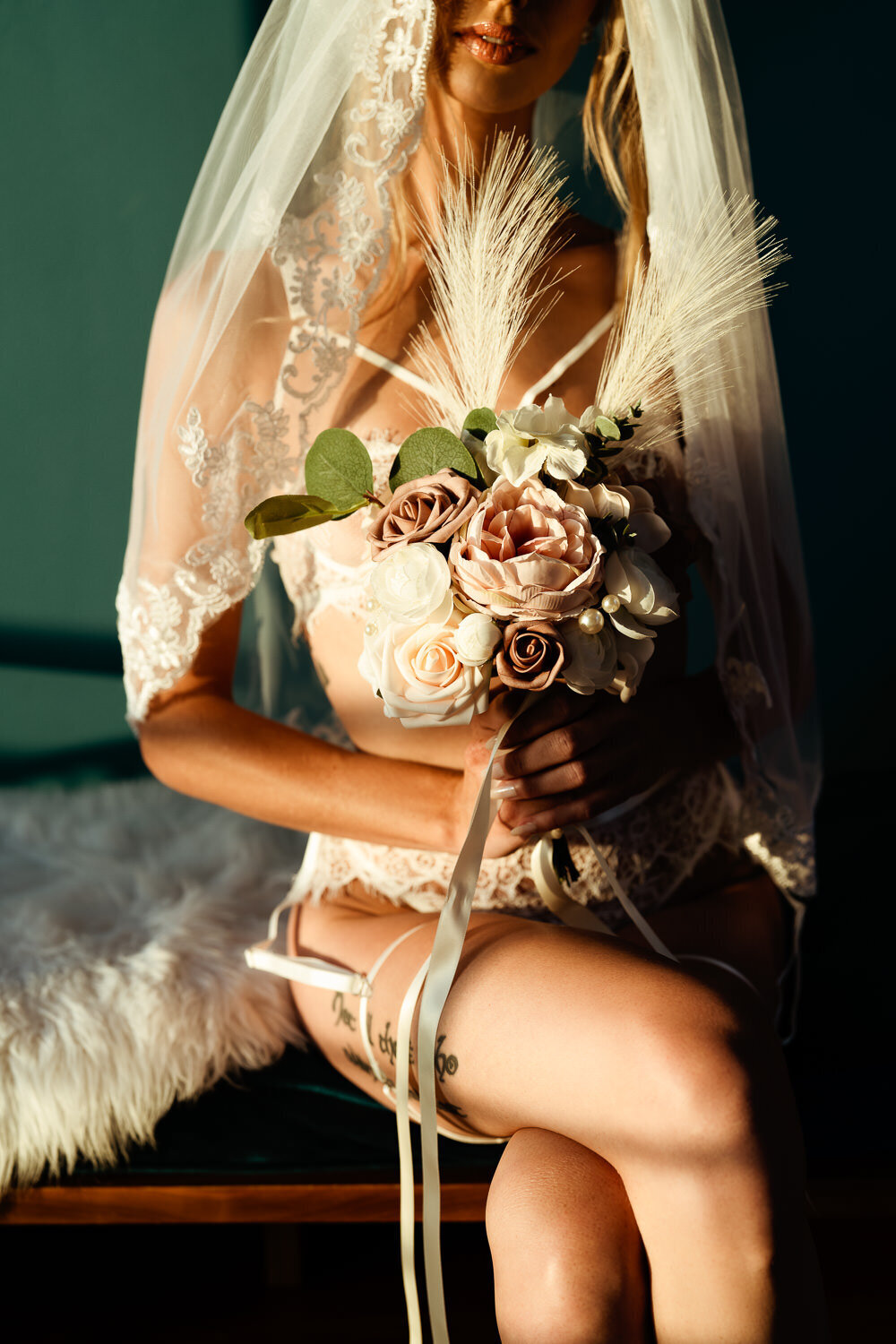 Bride in bridal lingerie holding bouquet and wearing veil during boudoir session on bench. Photographed by Art of You Boudoir in Round Rock, TX.