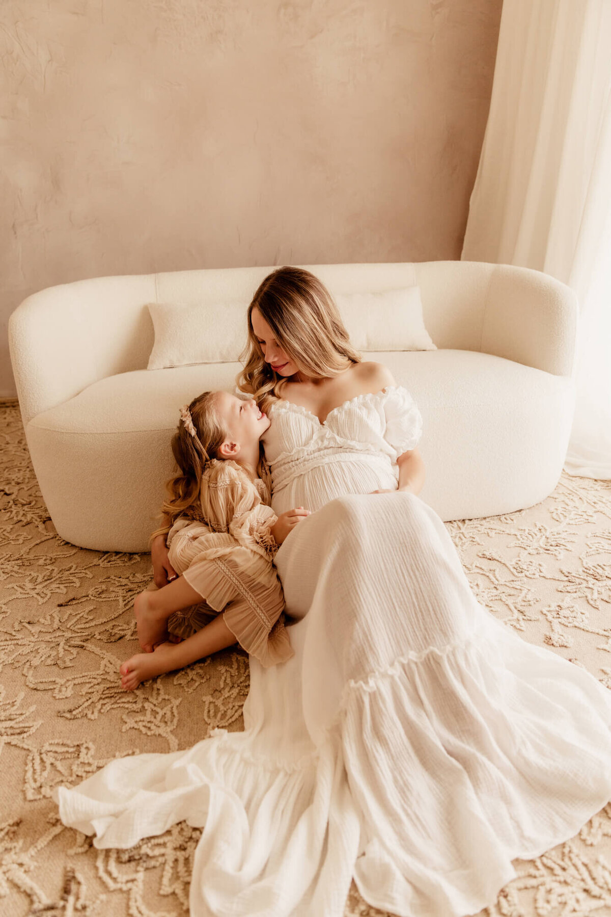 Mother and daughter smile at one another while sitting near a white modern curved couch in Yukon, Oklahoma.