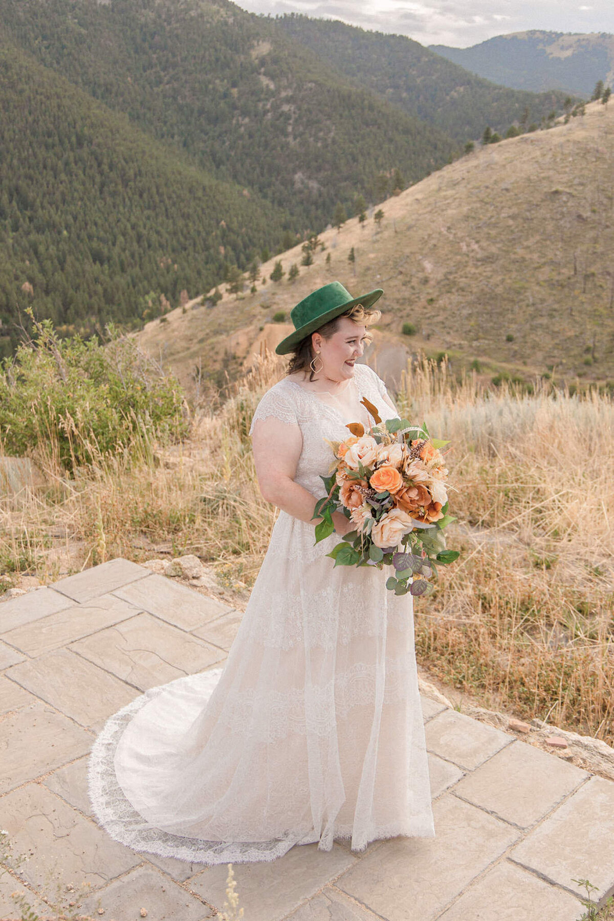 The bride, wearing a green hat and holding a stunning bouquet smiles at her off camera husband. Photographed by Stephanie Eddy, Colorado wedding photographer