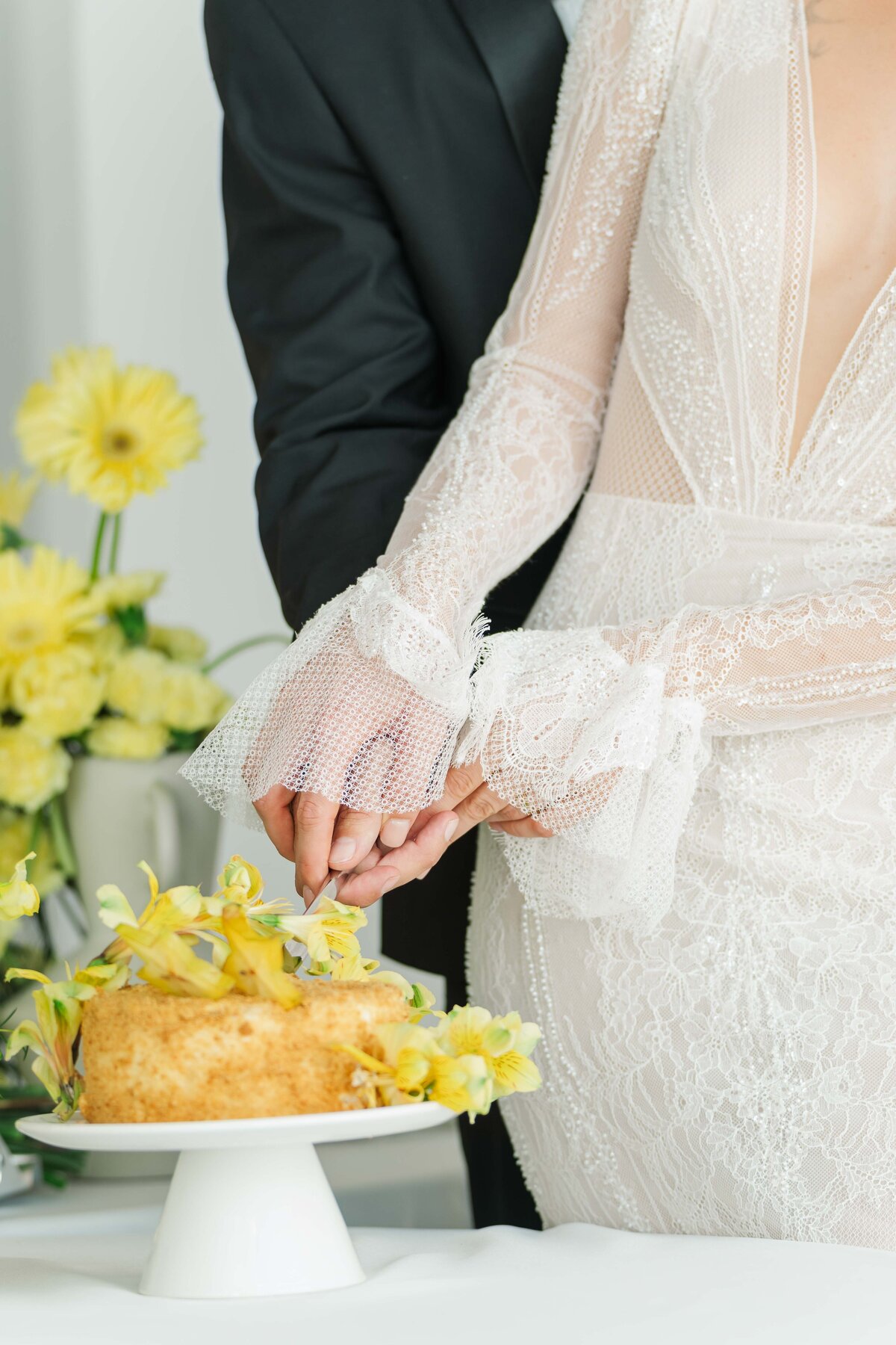 detail of a bride and groom's hands cutting their wedding cake