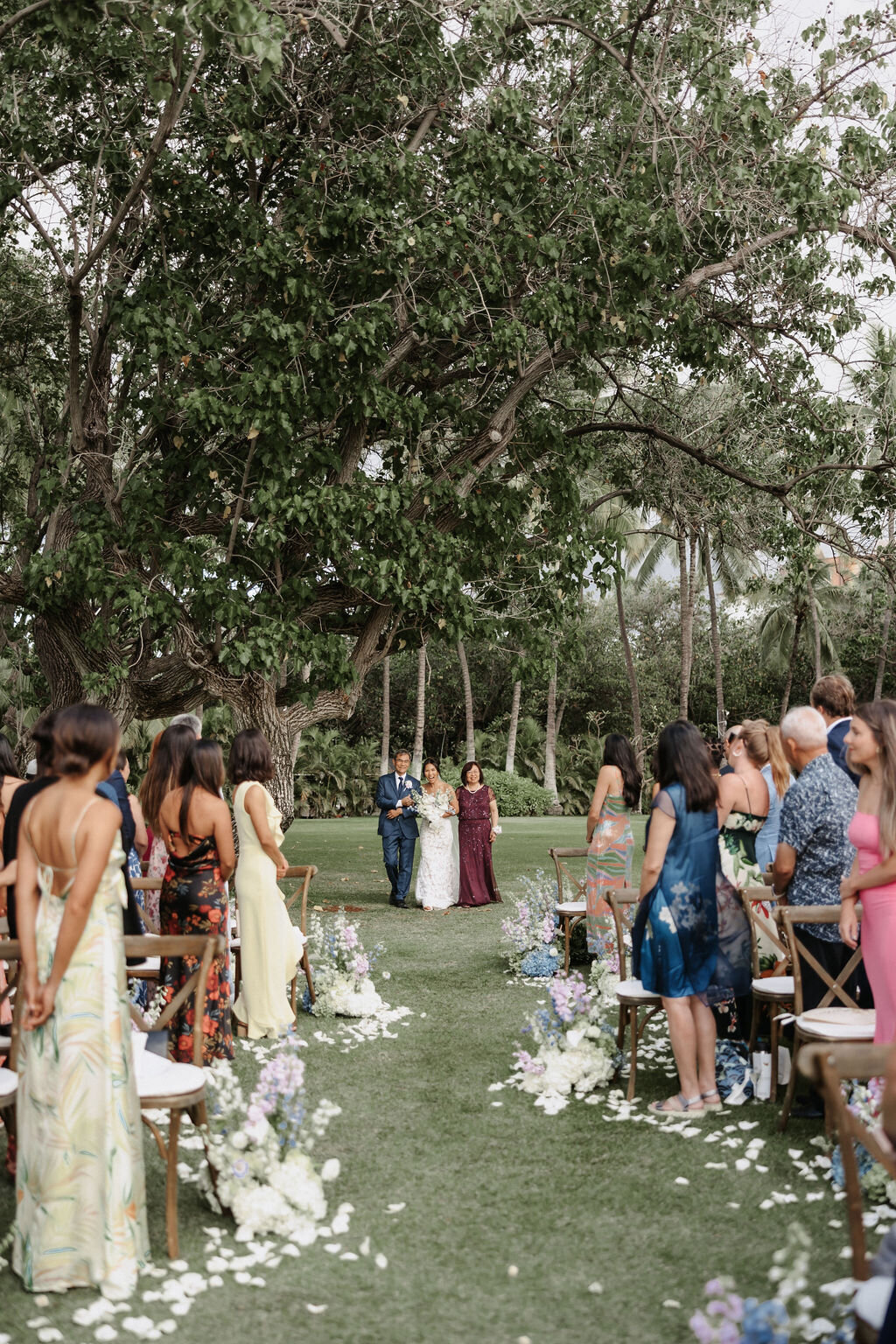 bride walking down winding aisle with parents as guests stand to watch at lanikuhonua koolina hawaii