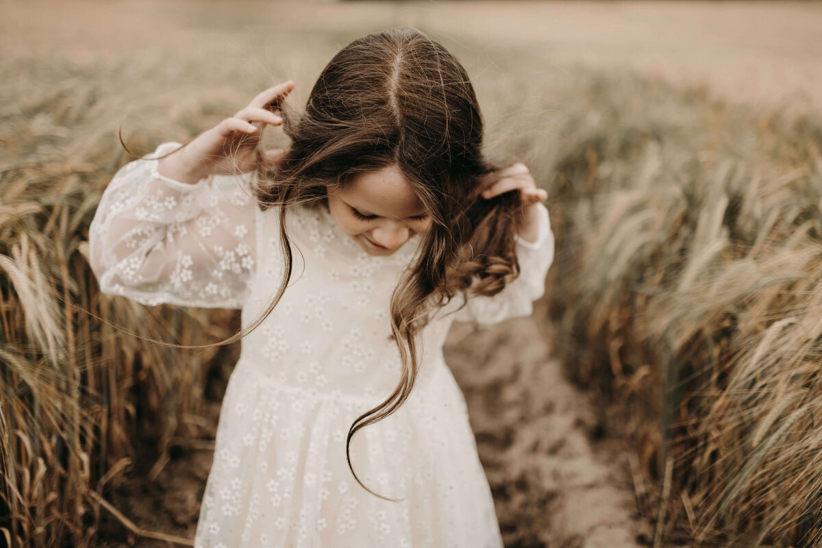 Charming image of a young girl in a lace dress twirling her hair in a field, captured by a Mullingar photographer