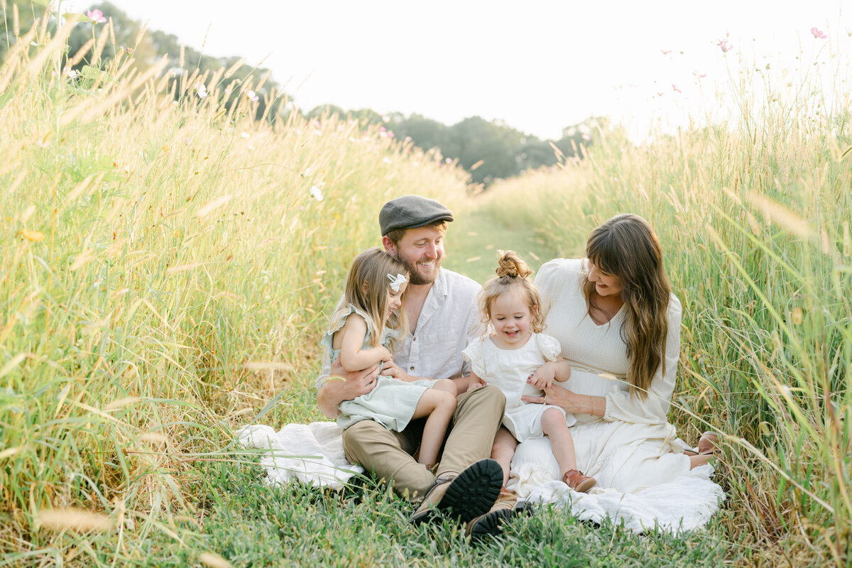 family in neutral clothing sits in a field of tall golden grass