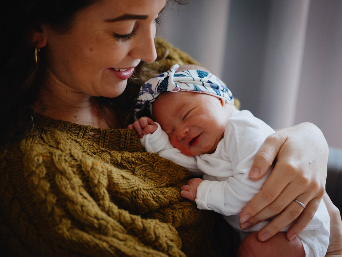A newborn baby girl rests on mom's cozy sweater and smiles.