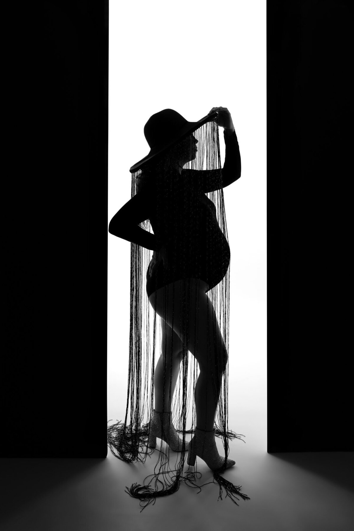 Backlit maternity silhouette of expecting couple against window during indoor photography session