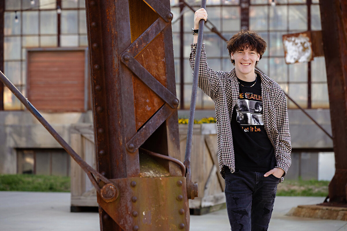 Editorial-style portrait of senior in Beatles shirt and checked button down, surrounded by industrial textures and mural art in Charlotte’s Camp North End.
