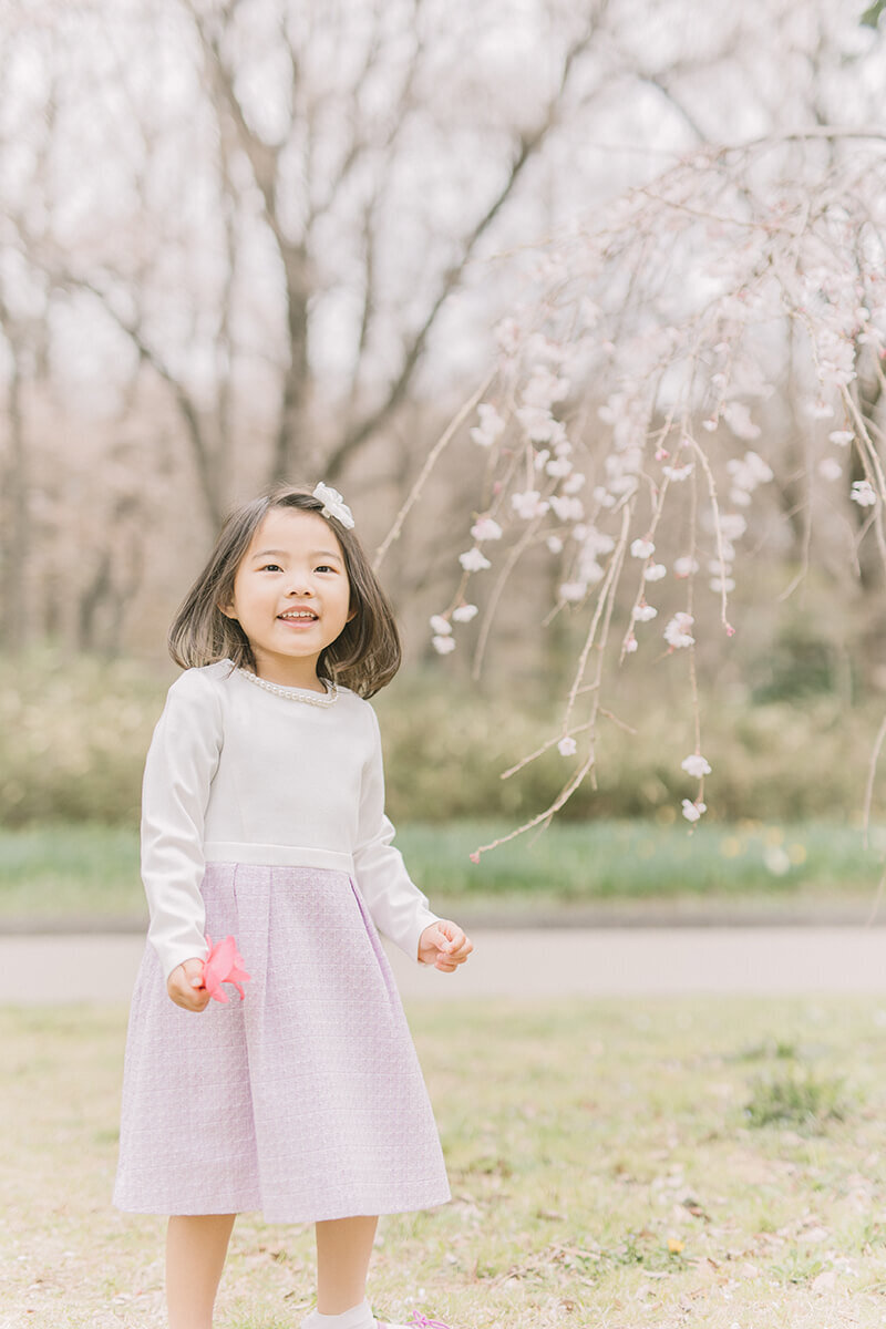 桜の木の前で空を見上げる女の子。淡い紫色のワンピースがオシャレ。